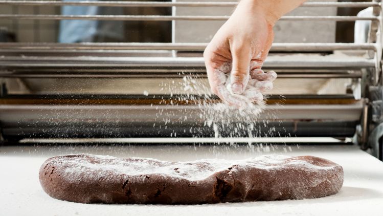 Hand sprinkling flour over chocolate dough in a bakery setting